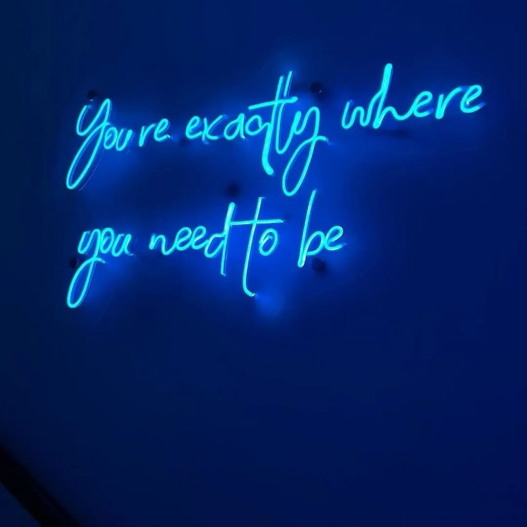 Zils neona uzraksts „You’re exactly where you need to be” uz studijas sienas
